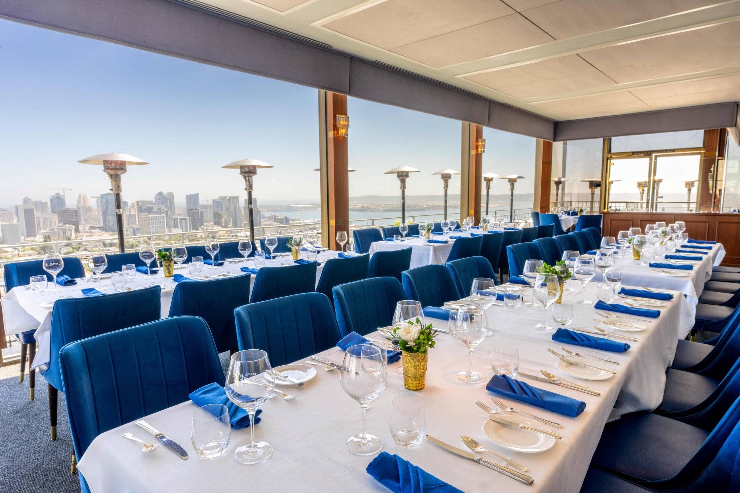 Banquet tables set in The Downtown Room at Mister A's with windows over downtown San Diego and the bay